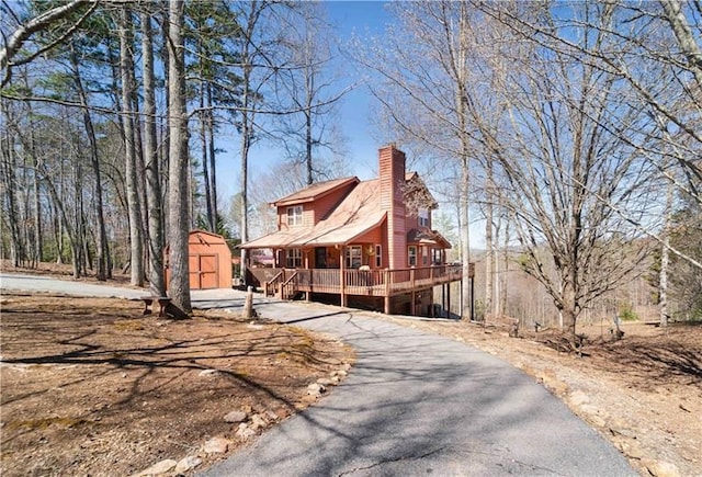 view of side of property with a wooden deck, a chimney, an outdoor structure, driveway, and a storage unit