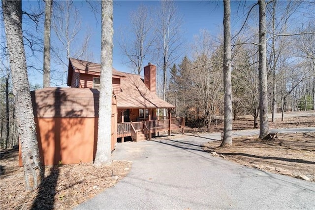 view of property exterior with a porch, a chimney, and driveway