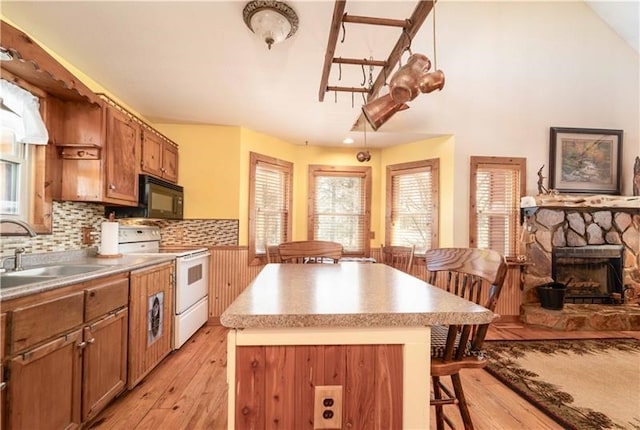 kitchen featuring a kitchen island, black microwave, white range with electric cooktop, a kitchen bar, and a sink