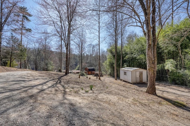 view of yard with an outdoor structure, a wooded view, and a shed