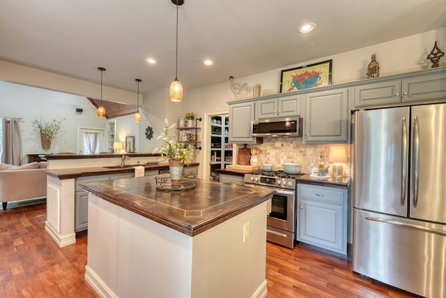 kitchen with decorative backsplash, appliances with stainless steel finishes, dark wood-type flooring, decorative light fixtures, and a kitchen island