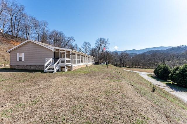 view of property exterior with a yard, a mountain view, and a sunroom