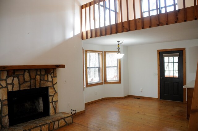 living room with light hardwood / wood-style floors, a stone fireplace, and a high ceiling