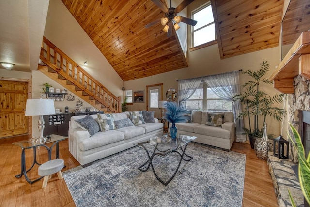 living room with wooden ceiling, high vaulted ceiling, a stone fireplace, light wood-type flooring, and ceiling fan