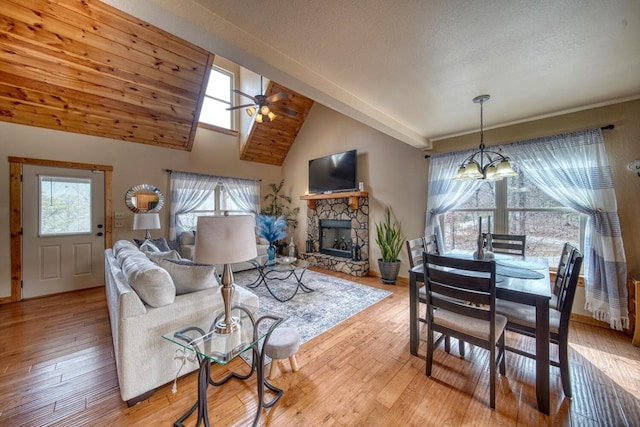 living room with ceiling fan with notable chandelier, a fireplace, light hardwood / wood-style floors, lofted ceiling with skylight, and a textured ceiling