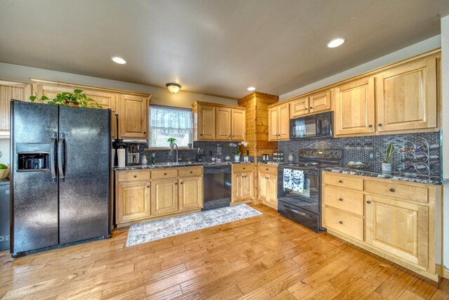 kitchen featuring backsplash, black appliances, light hardwood / wood-style floors, sink, and dark stone counters