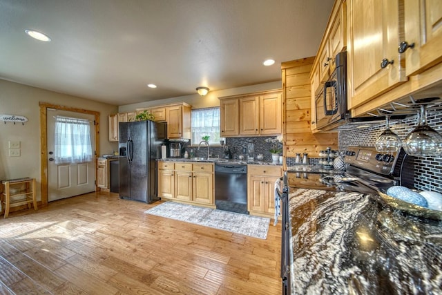 kitchen with backsplash, light wood-type flooring, dark stone countertops, and black appliances