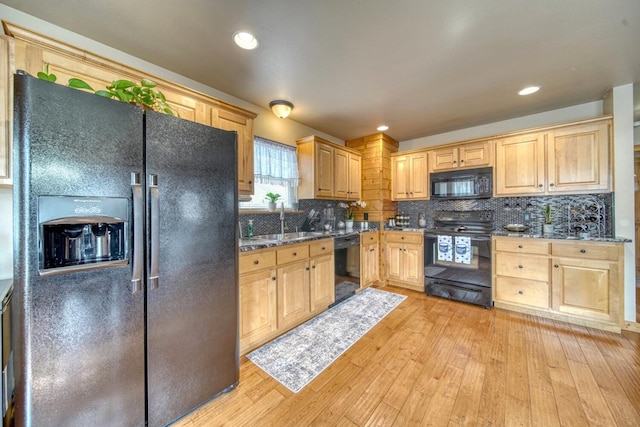 kitchen featuring tasteful backsplash, light brown cabinetry, dark stone countertops, light wood-type flooring, and black appliances