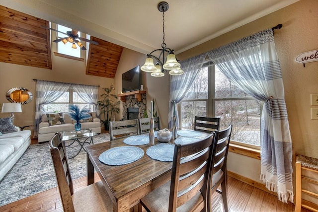 dining space featuring light wood-type flooring, lofted ceiling, a fireplace, ceiling fan with notable chandelier, and wood ceiling