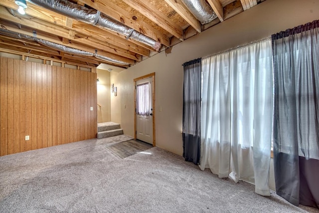 carpeted empty room featuring wood walls and beamed ceiling