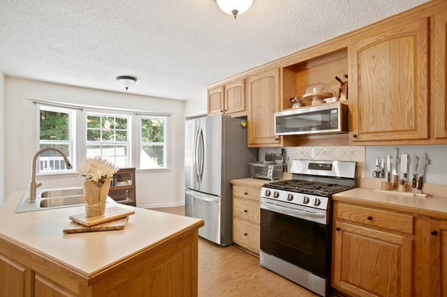 kitchen with sink, appliances with stainless steel finishes, a textured ceiling, and light hardwood / wood-style floors