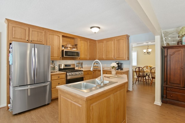 kitchen with appliances with stainless steel finishes, sink, light wood-type flooring, an island with sink, and hanging light fixtures