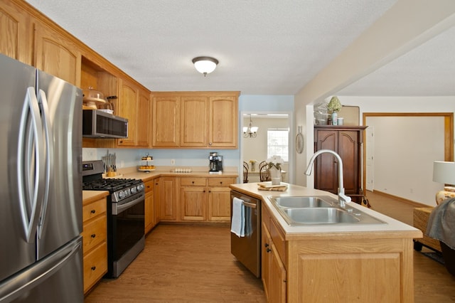 kitchen with a kitchen island with sink, light hardwood / wood-style flooring, sink, appliances with stainless steel finishes, and a textured ceiling