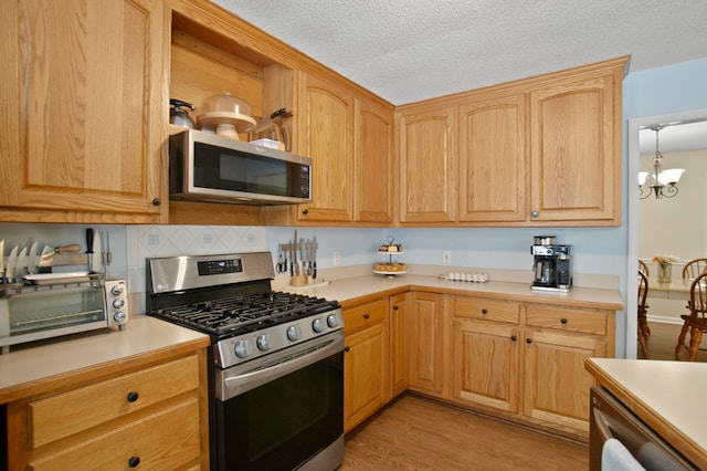 kitchen with light wood-type flooring, a textured ceiling, hanging light fixtures, stainless steel appliances, and an inviting chandelier