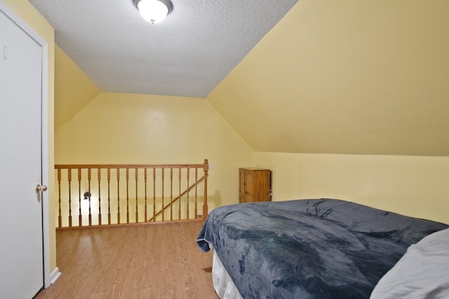 bedroom with a textured ceiling, vaulted ceiling, and light wood-type flooring