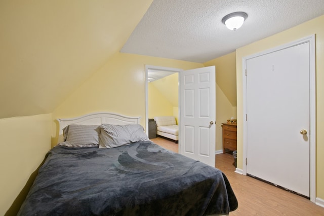 bedroom with a textured ceiling, light wood-type flooring, and vaulted ceiling