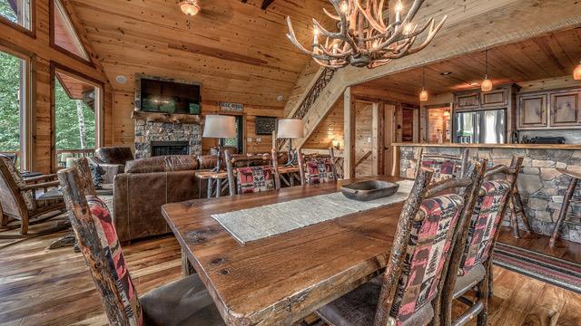 dining area featuring wood-type flooring, a stone fireplace, wooden walls, a notable chandelier, and vaulted ceiling