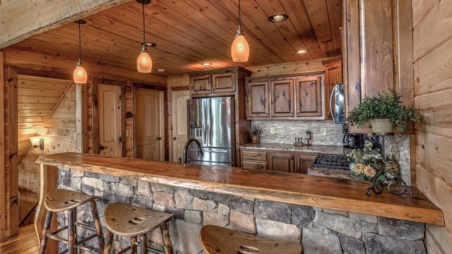 bar featuring pendant lighting, stainless steel appliances, wooden ceiling, hardwood / wood-style flooring, and wooden walls