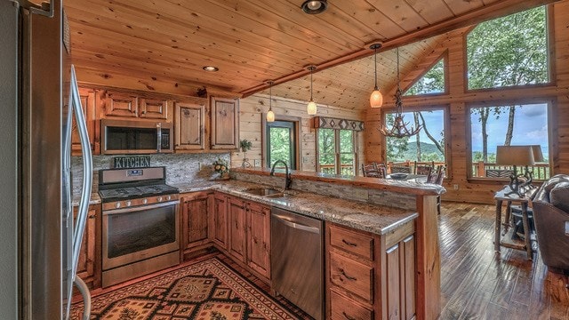 kitchen featuring dark wood-type flooring, kitchen peninsula, pendant lighting, stainless steel appliances, and lofted ceiling