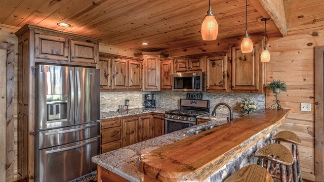 kitchen with dark stone counters, wooden walls, kitchen peninsula, and appliances with stainless steel finishes