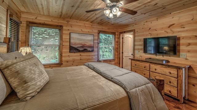 bedroom with wooden walls, multiple windows, hardwood / wood-style floors, and ceiling fan