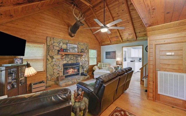 living room with wood-type flooring, ceiling fan, vaulted ceiling with beams, wooden ceiling, and a stone fireplace