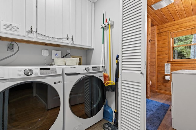 laundry area with dark wood-type flooring, wooden walls, cabinets, and washing machine and dryer