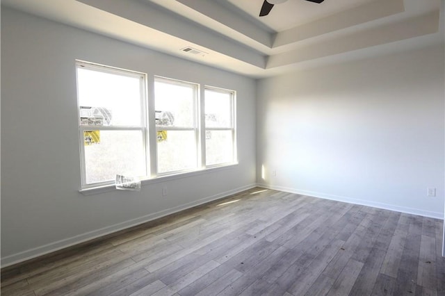 empty room with a tray ceiling, ceiling fan, dark wood finished floors, and baseboards