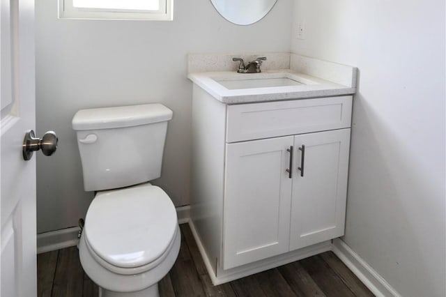 bathroom with toilet, vanity, wood finished floors, and baseboards