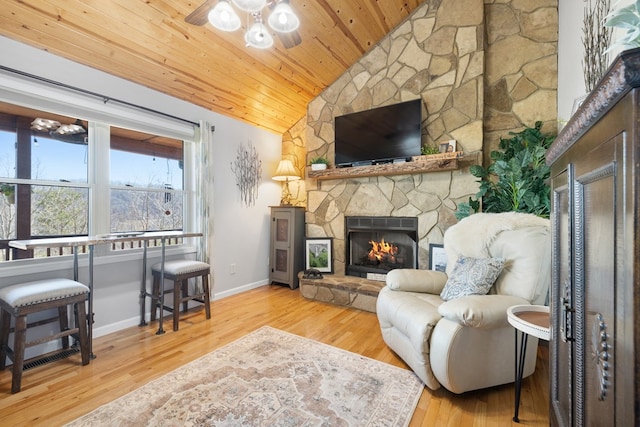 living room with a stone fireplace, lofted ceiling, wood finished floors, and ceiling fan