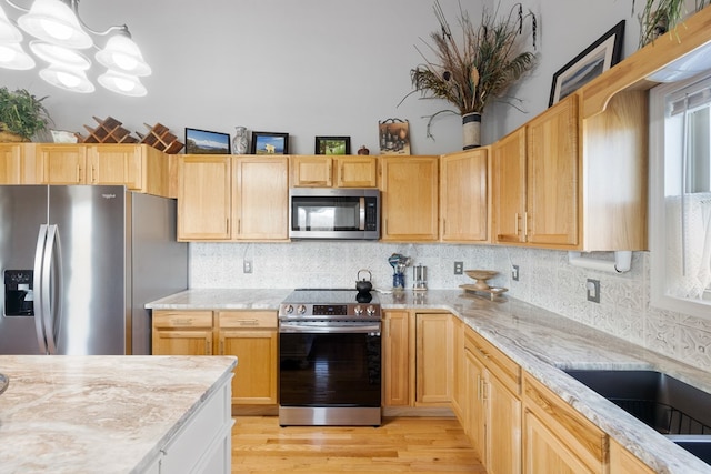 kitchen with light wood-type flooring, stainless steel appliances, an inviting chandelier, and decorative backsplash