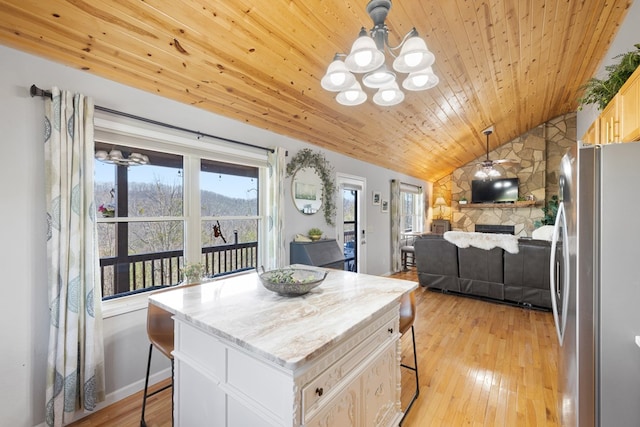 kitchen with light wood-type flooring, vaulted ceiling, a kitchen breakfast bar, freestanding refrigerator, and a notable chandelier