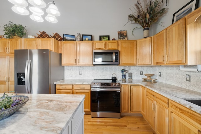 kitchen with decorative backsplash, light stone countertops, light wood-style floors, and appliances with stainless steel finishes