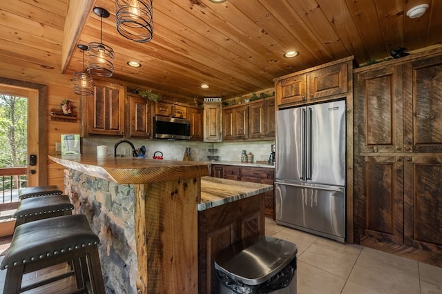 kitchen featuring stainless steel appliances, kitchen peninsula, wooden walls, light tile patterned floors, and a breakfast bar