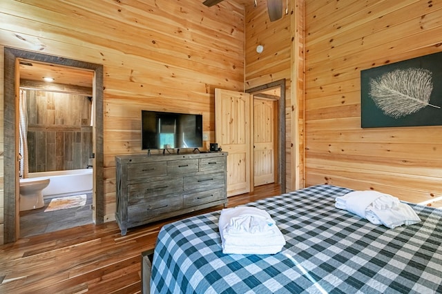 bedroom featuring wood walls, hardwood / wood-style flooring, ceiling fan, and connected bathroom