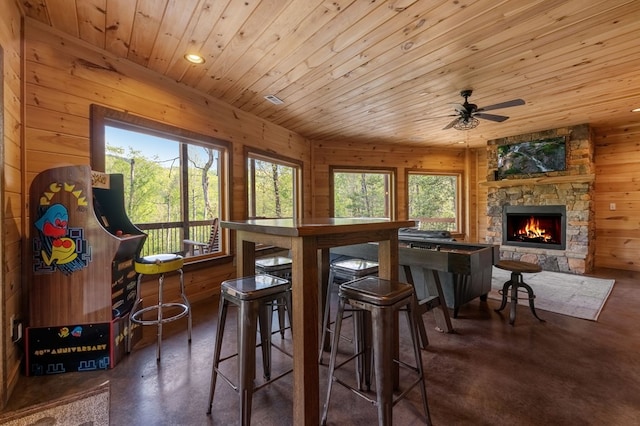 interior space featuring a stone fireplace, wooden walls, wooden ceiling, and plenty of natural light