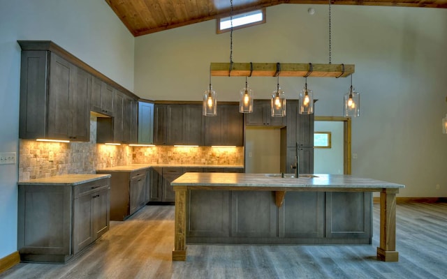 kitchen with decorative backsplash, high vaulted ceiling, pendant lighting, light hardwood / wood-style floors, and a center island