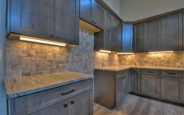 kitchen with gray cabinetry, light hardwood / wood-style floors, tasteful backsplash, and light stone counters