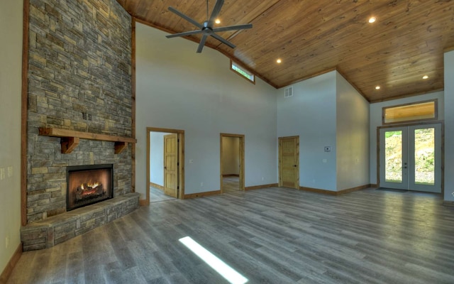 unfurnished living room with ceiling fan, high vaulted ceiling, wooden ceiling, a stone fireplace, and french doors