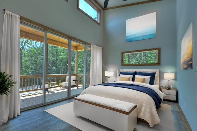 bedroom with a towering ceiling, multiple windows, access to outside, and hardwood / wood-style flooring