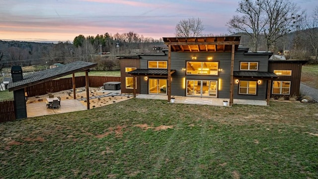 rear view of house with a standing seam roof, a hot tub, a lawn, and a patio