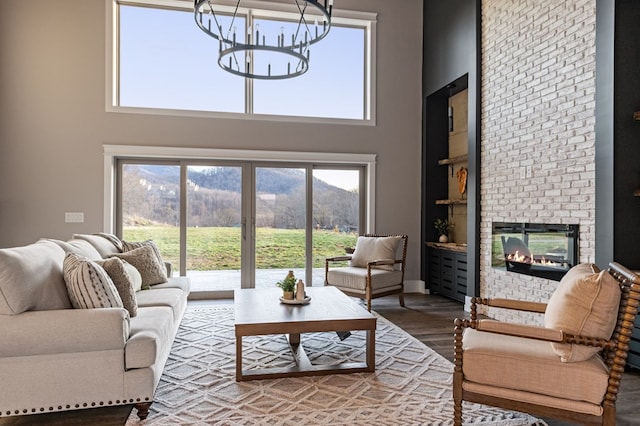 living room featuring a towering ceiling, a brick fireplace, a mountain view, wood finished floors, and a chandelier