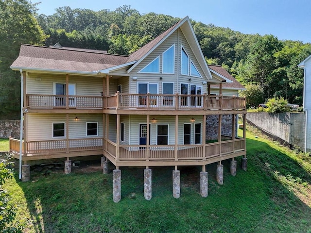 back of house featuring roof with shingles, a lawn, a forest view, and fence