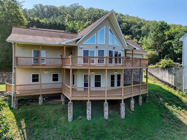 rear view of property featuring a yard, roof with shingles, a forest view, and fence