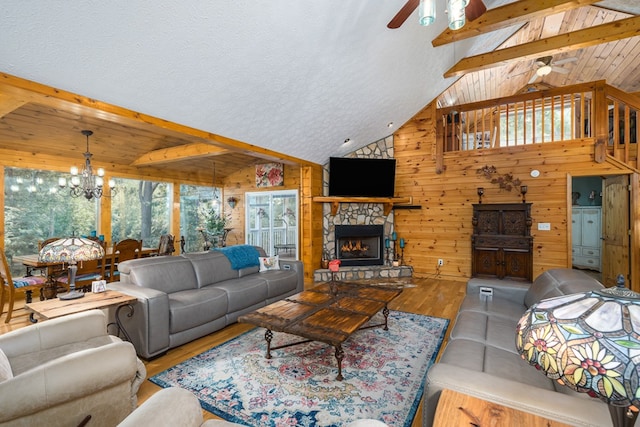 living room with vaulted ceiling with beams, wooden walls, ceiling fan with notable chandelier, a fireplace, and wood finished floors