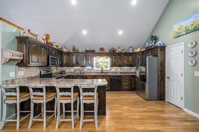 kitchen with a breakfast bar, stainless steel appliances, a sink, dark brown cabinetry, and a peninsula