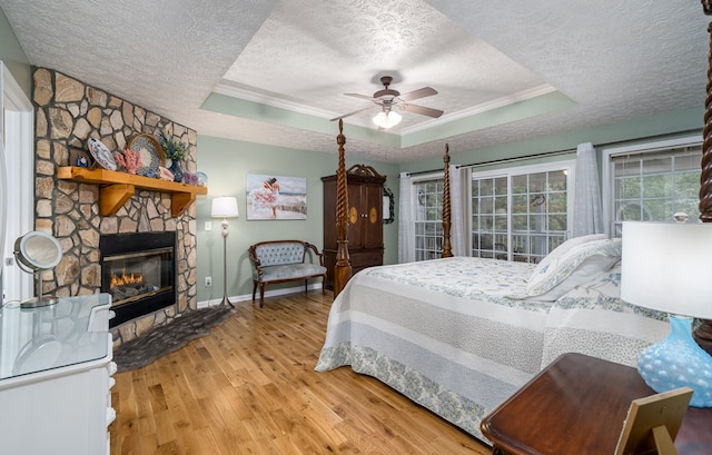 bedroom with a tray ceiling, a fireplace, a textured ceiling, and wood finished floors