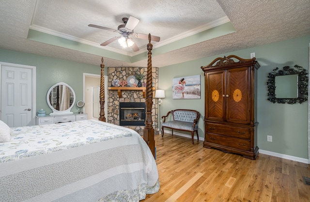 bedroom with a textured ceiling, a tray ceiling, light wood-type flooring, and ornamental molding