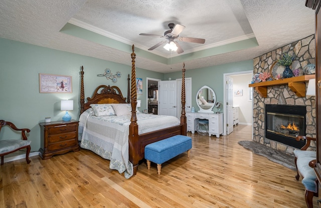 bedroom with light wood-type flooring, a tray ceiling, a textured ceiling, and a stone fireplace