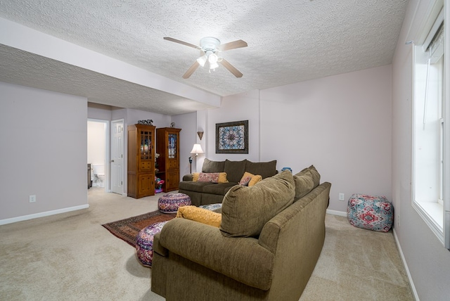 living area featuring light carpet, ceiling fan, a textured ceiling, and baseboards